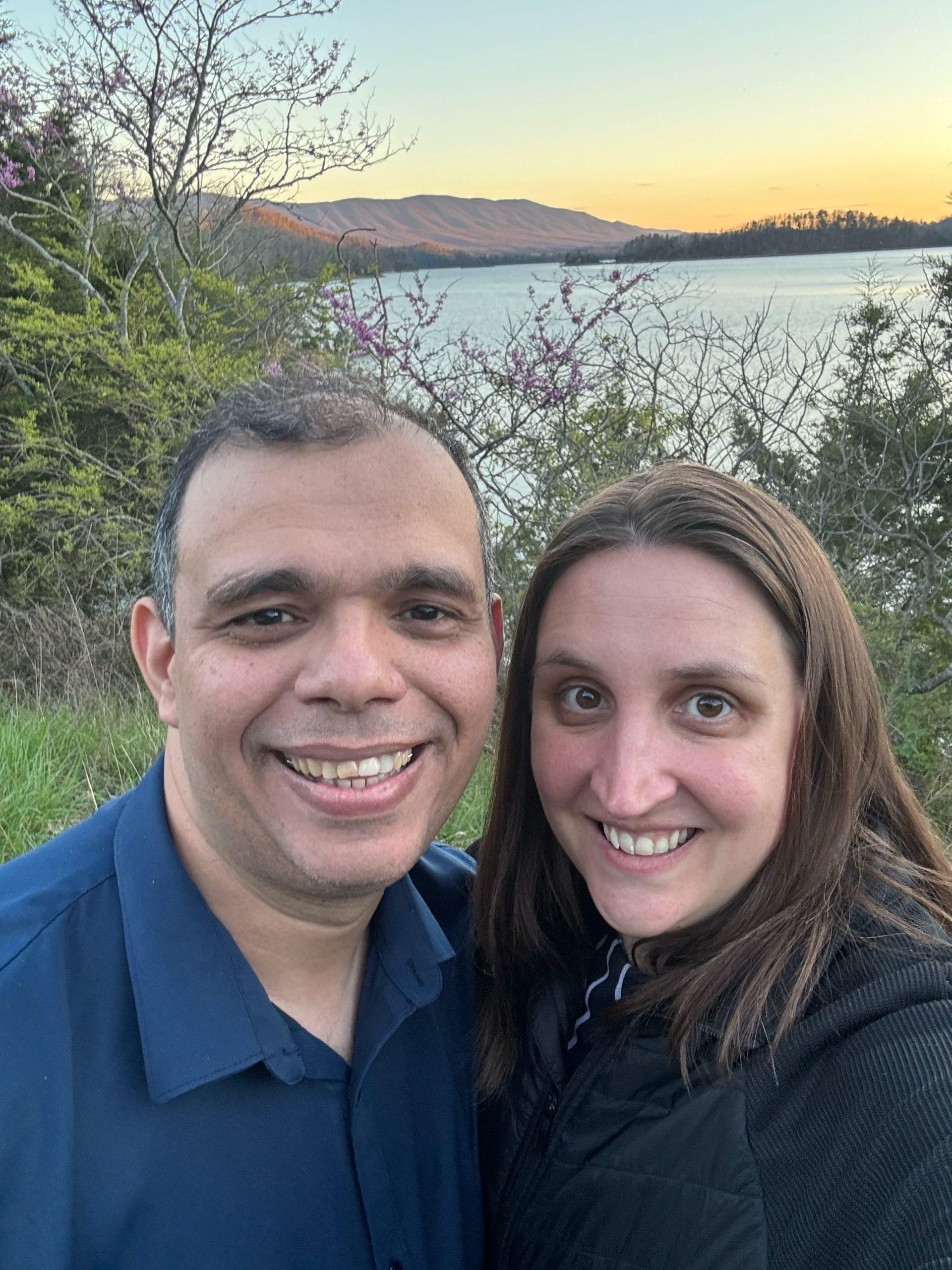 Samantha and her husband smiling together outdoors at sunset by a lake in North Carolina